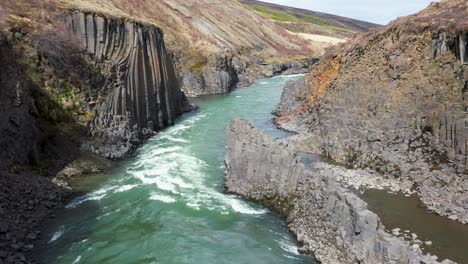 Drone-flight-over-a-turquoise-river-flowing-through-a-basalt-column-canyon-in-Iceland