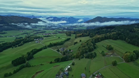-green-valley-with-scattered-houses,-low-clouds-over-distant-mountains-at-dusk-in-austria