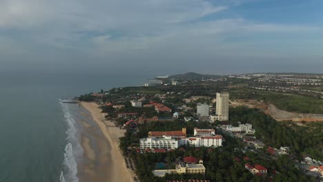 Morning-aerial-orbit-shot-of-resorts-in-Mui-ne,-Vietnam-in-golden-light-featuring-swimming-pools,-beach,-buildings-and-gardens