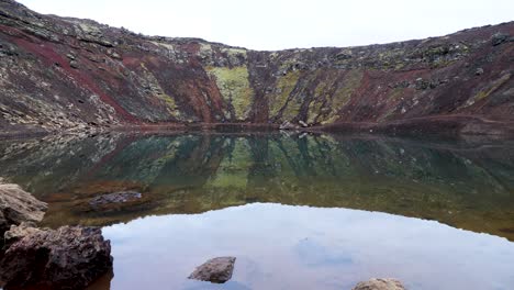 Tranquil-volcanic-crater-lake-in-Iceland-with-steep,-colorful-slopes-and-clear-reflection-in-the-water