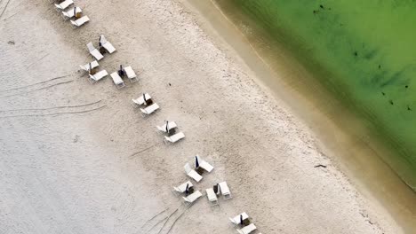 sliding-diagonal-view-of-close-up-to-empty-lounge-chairs-with-the-waves-coming-to-sand-at-Rosmery-Beach-FL