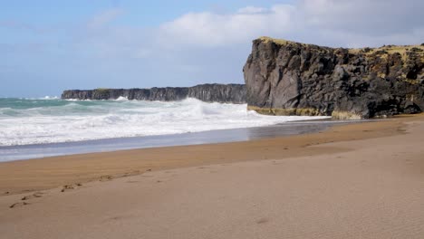 Ruhiger-Isländischer-Strand-Mit-Schroffen-Klippen-Und-Wellen,-Die-Am-Ufer-Brechen,-Fußspuren-Im-Sand-Weisen-Auf-Kürzliche-Besucher-Hin