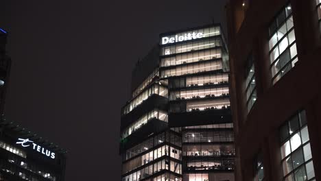Tight-parallax-reveal-looking-up-at-tall-skyscrapers-in-the-city-of-Vancouver-at-night-with-each-floor-lit-up-and-business-names-Deloitte-and-Telus-on-the-building