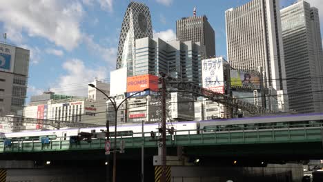 An-Einem-Sonnigen-Tag-Fährt-Ein-U-Bahn-Zug-Auf-Einer-Hochbahnstrecke-Vorbei,-Im-Hintergrund-Ist-Das-Gebäude-Mit-Dem-Stadtbild-Von-Shinjuku-Zu-Sehen