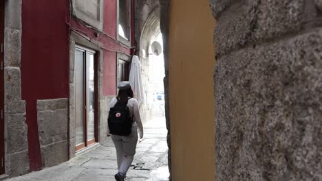 Dolly-left-shot-revealing-woman-walking-down-traditional-covered-narrow-street,-Porto