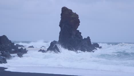 Dramatische-Wellen-Schlagen-Gegen-Einzigartige-Felsformationen-An-Einem-Schwarzen-Sandstrand-In-Island-Unter-Bewölktem-Himmel
