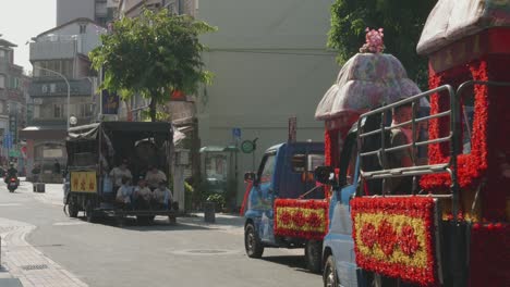 Parade-of-traditional-shrines-loaded-on-compact-trucks-in-Asia-drive-down-road-in-city