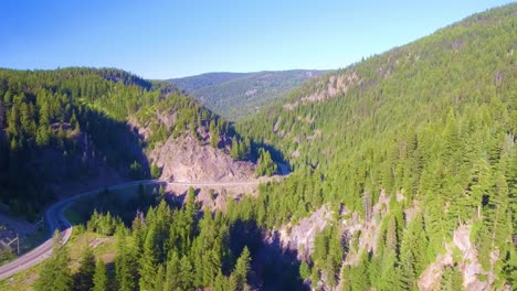 Push-in-drone-shot-in-the-boreal-forest-of-British-Columbia-showcasing-the-rocky-mountains-with-a-winding-highway-on-a-bright-sunny-day