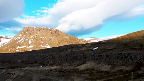 Rugged-Icelandic-mountain-landscape-under-a-blue-sky-with-floating-clouds,-drone-shot