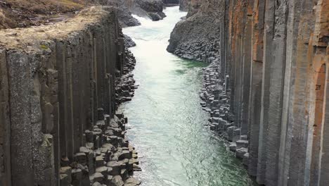Luftaufnahme-Eines-Turbulenten-Flusses,-Der-Durch-Eine-Dramatische-Basaltsäulenschlucht-In-Der-Kahlen-Isländischen-Landschaft-Fließt