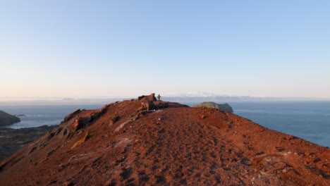 Un-Anciano-Excursionista-En-La-Cresta-Volcánica-Roja-Con-Vistas-Panorámicas-Del-Océano-En-Islandia