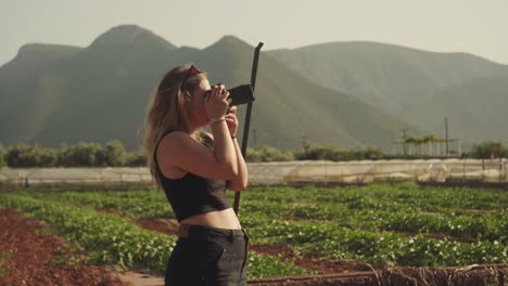 Static,-woman-holds-camera-with-telephoto-lens-to-eye-as-wind-blows-slowly-on-Leonidio,-Greece-countryside