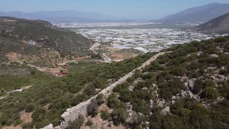 Drone-panning-from-the-bottom-going-up,-showing-the-wall-along-the-Lycian-Way's-hiking-trail-and-a-modern-Turkish-town-in-Antalya-province-in-Turkey