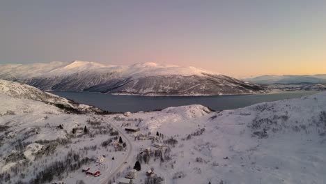 Un-Dron-Aéreo-Disparó-Sobre-Una-Cadena-Montañosa-Llena-De-Nieve-Que-Rodea-Un-Lago-Durante-Una-Mañana-De-Invierno-Al-Amanecer-En-Ersfjordvegen,-Noruega