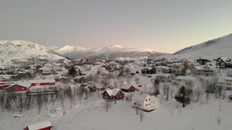 Aerial-rising-shot-of-a-small-village-with-snow-covered-mountains-behind