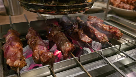 Auto-Turning-Skewers,-Lamb-BBQ-Cooking-Automation---Lamb-Meat-on-Skewers-Roasted-on-Live-Coals-Automatically-Spun-With-an-Electric-Machine-For-Even-Roast-in-Korean-Restaurant---Close-up
