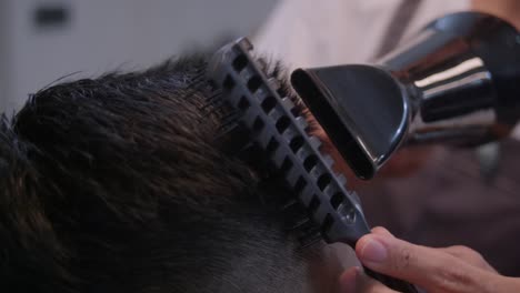 Black-hair-dryer-and-black-comb-driven-through-top-of-head-with-black-hair,-filmed-as-closeup-shot-in-slow-motion-handheld-style