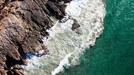 Bird's-Eye-View-Of-Waves-Splashing-On-Rugged-Cliffs-In-Noosa,-Queensland,-Australia---Drone-Shot