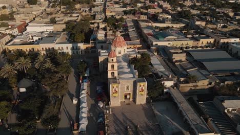 Aerial-View-of-a-church-next-to-a-square-with-palm-trees-in-a-peaceful-Mexican-town-at-dawn