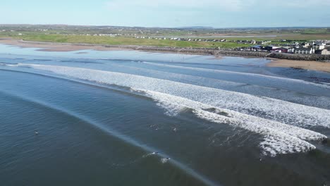 Aerial-tracking-shot-of-surfers-riding-a-large-wave-at-Lahinch-Beach,-Ireland