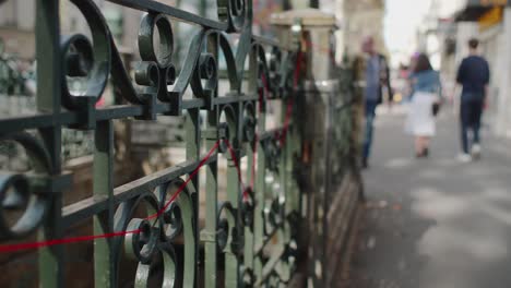 Follow-Shot-Along-Railings-With-Red-Thread-Beside-Metro-Entrance-With-People-Walking-Past-In-Paris