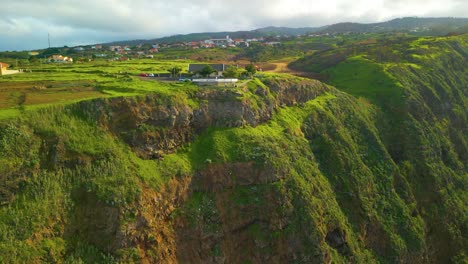 Aerial-view-of-house-in-green-cliff-on-Madeira-Island-during-sunny-day,-Portugal---orbiting-shot