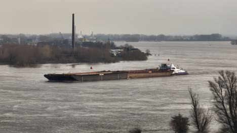 Aerial-close-up-of-a-tug-pushing-a-barge-down-the-flooded-Waal-river-near-Slot-Loevestein,-Gorinchem-Netherlands-in-the-winter-of-2024-after-heavy-rains-fall-over-Northern-Europe