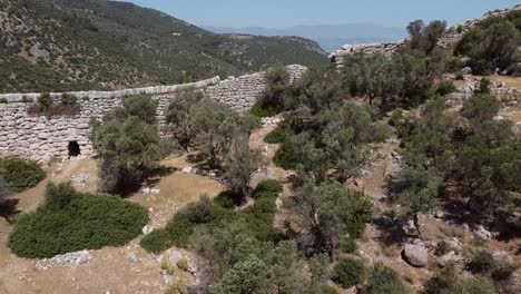 Pedestal-drone-shot-moving-from-the-bottom-going-up,-showing-a-wall-along-the-Lycian-Way's-hiking-trail-and-revealing-a-modern-Turkish-town-below,-located-in-the-province-of-Antalya,-Turkey