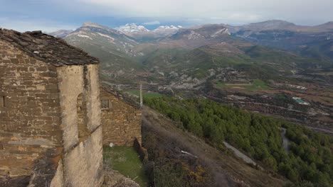 Drone-shot-from-an-abandoned-church-in-Muro-de-Bellos,-Spain-with-a-beautiful-green-landscape-and-a-snowy-mountain-as-a-background
