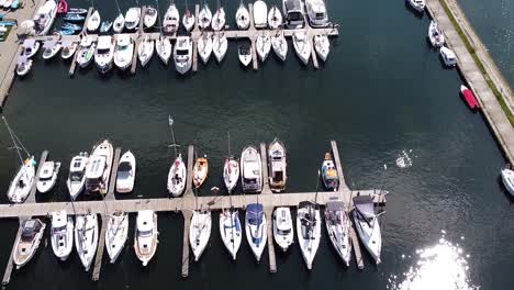Sun-reflecting-on-lake-water-in-local-marina-with-many-yachts,-aerial-view