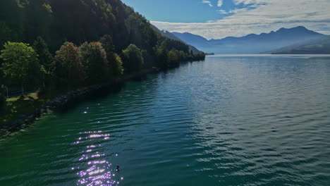 Stunning-drone-shot-of-Attersee-Lake-in-Austria-with-woodland-shores-and-hazy-mountains