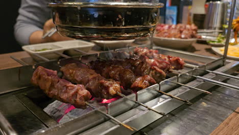 Eingebauter-Holzkohlegrilltisch-Mit-Automatisch-Drehenden-Spießen,-Lammfleisch-Grill-Wird-Von-Besuchern-Eines-Koreanischen-Restaurants-Zubereitet-–-Nahaufnahme