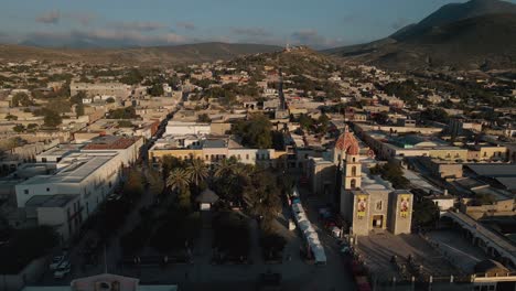 Aerial-panoramic-view-over-a-Mexican-town-center-with-a-church-and-a-square-with-palm-trees