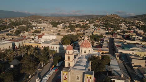 Aerial-View-of-a-church-in-a-peaceful-mexican-town-at-dusk-with-green-hill-in-the-background