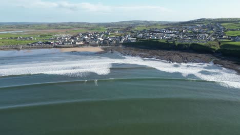 Aerial-orbiting-shot-of-surfers-cathing-waves-at-Lahinch-Beach-on-a-summers-day