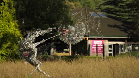Wire-Fairy-Holding-A-Dandelion-Is-Slowly-Rotating-In-The-Wind-On-The-Meadow-At-The-Main-Entrance-Of-Trentham-Estate-Gardens