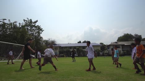 Fröhliche-Thailändische-Schulkinder,-Die-Fußball-Spielen,-Auch-Bekannt-Als-Fußball,-Und-Tore-Schießen,-Filmische-Zeitlupenansicht