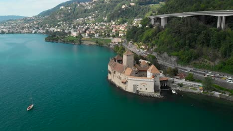 Aerial-Orbit-Movement-of-Chillon-Castle-with-Sailing-Boat-and-Busy-Road