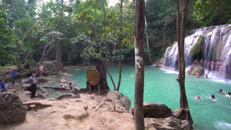 Gente-Disfrutando-De-Aguas-Turquesas-En-La-Laguna-De-La-Piscina-Natural-Bajo-Una-Exótica-Cascada-Tropical-En-La-Selva-Tropical-Del-Parque-Nacional-De-Erawan,-Tailandia