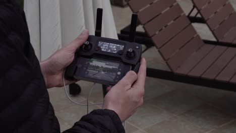 Close-Up-of-Male-Hands-Holding-DJI-Drone-Remote-Controiler-and-Smartphone-as-Screen