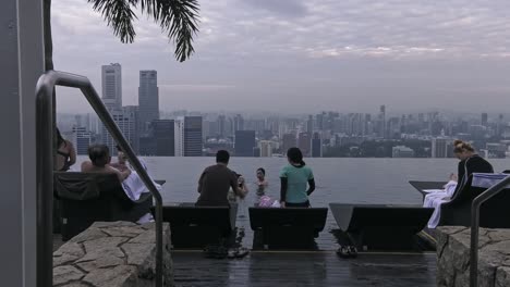 Tourists-relaxing-on-lounge-chairs-near-rooftop-infinity-pool-of-Marina-Bay-Sands-Hotel-SkyPark,-in-Singapore---Medium-wide-static-shot