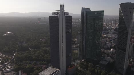 Vista-Aérea-De-Los-Rascacielos-De-La-Ciudad-De-México-En-El-Distrito-Financiero-Del-Centro-Y-Una-Línea-Brumosa-En-Una-Tarde-Soleada,-Disparo-De-Drones