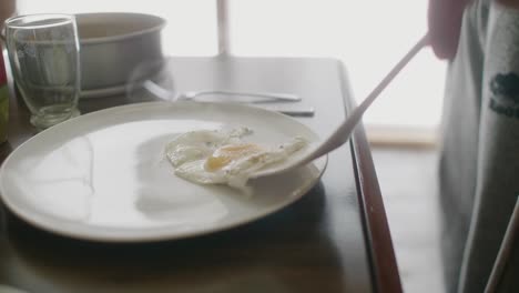 Fried-Egg-With-Pepper-Being-Laid-On-Plate-From-Spatula