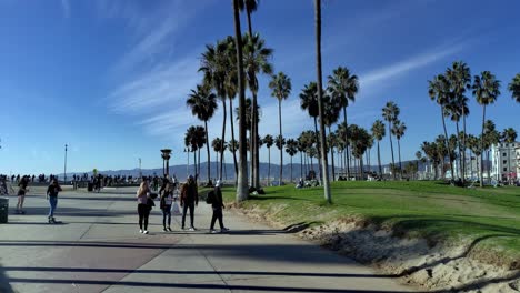 Venice-Beach-Boardwalk-in-the-afternoon-with-people-walking-around-and-shopping-in-the-background-in-Los-Angeles,-California,-USA---slow-panning-shot