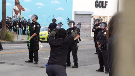 Mann-Mit-Erhobenen-Händen-Vor-Der-Polizeiblockade-In-Los-Angeles,-Kalifornien,-USA-Während-Des-Black-Lives-Matter-Protestes,-Gummigeschosse,-Ersatzeinheit-Im-Hintergrund,-Zeitlupe