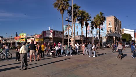 People-wearing-masks-and-gathering-outdoors-to-watch-a-show-at-the-Venice-Beach-Boardwalk-during-covid-19-pandemics-in-Los-Angeles,-California,-USA