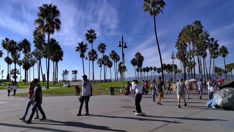 Entrance-to-the-Venice-Beach-Boardwalk-surrounded-by-people-walking-around-and-shops-and-performers-in-the-background-in-Los-Angeles,-California,-USA