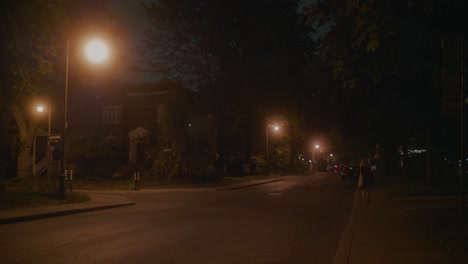 Einsame-Frau,-Die-Eine-Leere,-Von-Orangefarbenen-Straßenlaternen-Beleuchtete-Straße-In-Montreal-Entlang-Geht