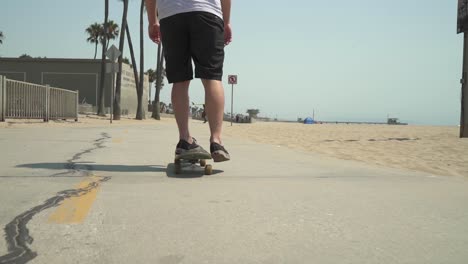 Close-up-following-shot-of-skateboarder-riding-on-sidewalk-in-Venice-Beach,-CA
