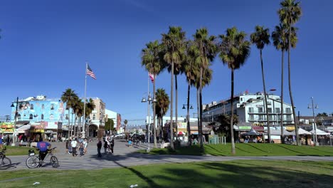 Gente-Deambulando-Por-El-Paseo-Marítimo-De-Venice-Beach-Con-Imponentes-Palmeras-Desde-Windward-Plaza-En-Venice,-Los-Ángeles,-California